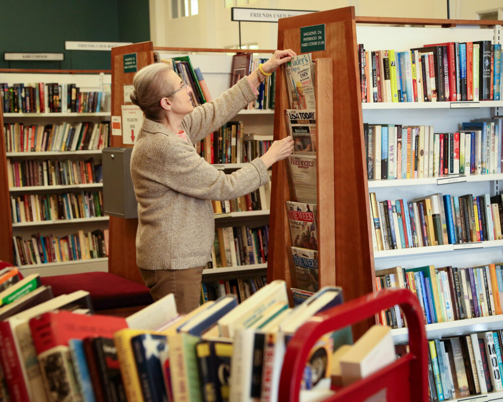 a women organizes magazines on a shelf surrounded by books